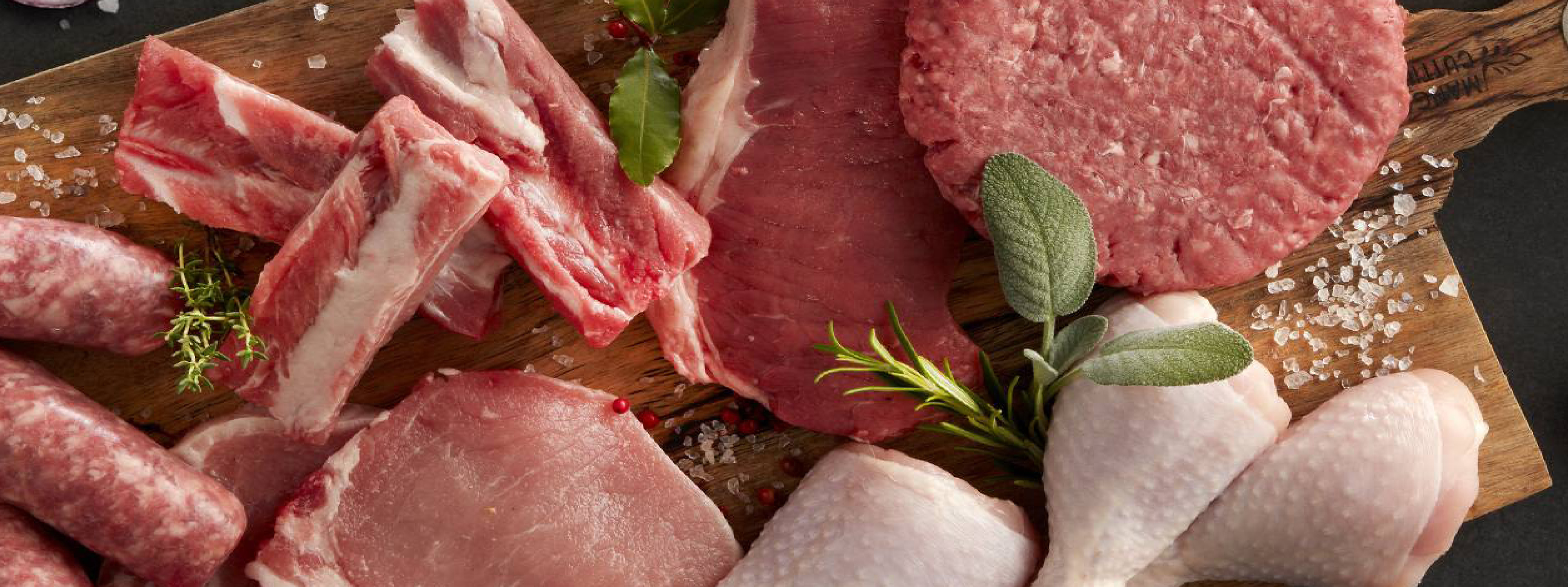Assortimento di carne fresca su tagliere di legno: costolette, bistecche, hamburger, cosce di pollo.