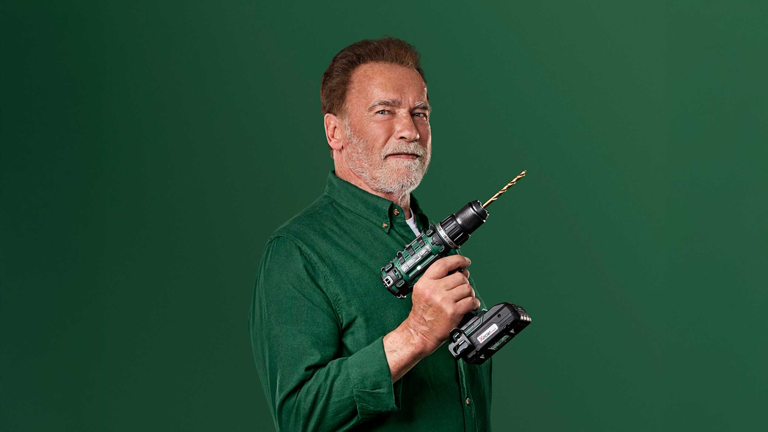 Arnold Schwarzenegger tiene un trapano a batteria verde con una punta dorata.