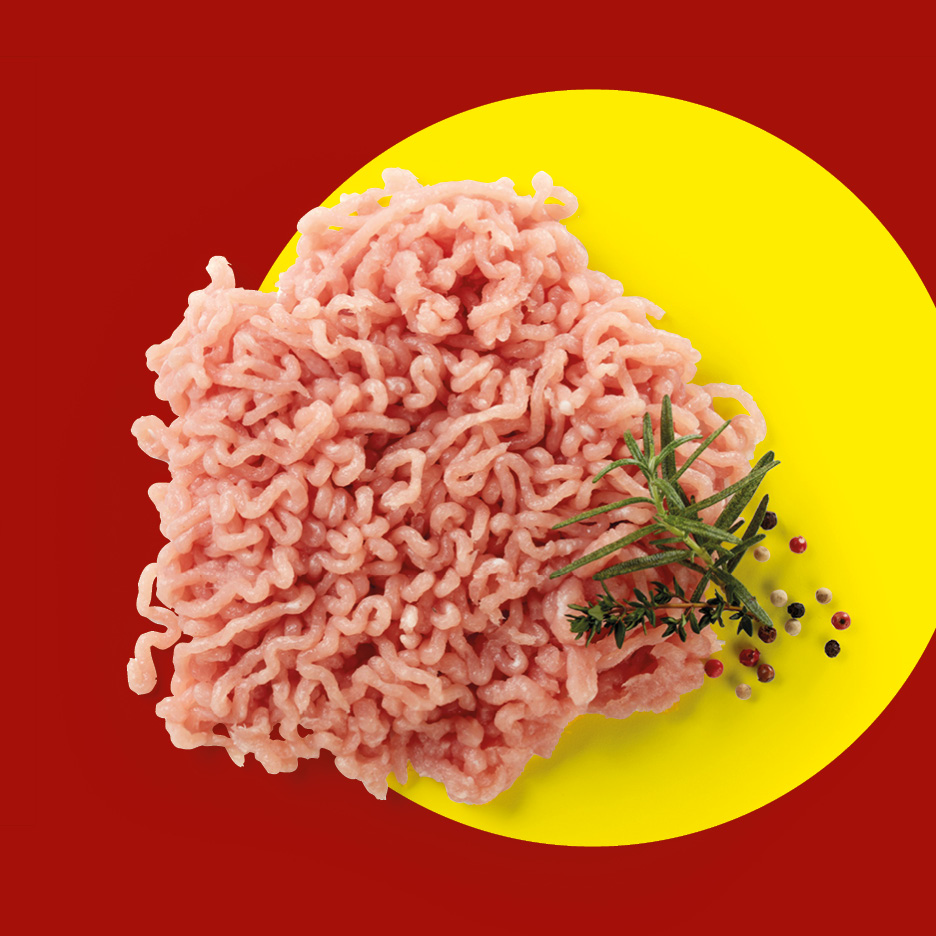 Carne macinata di pollo o tacchino con rosmarino e grani di pepe su sfondo giallo e rosso.