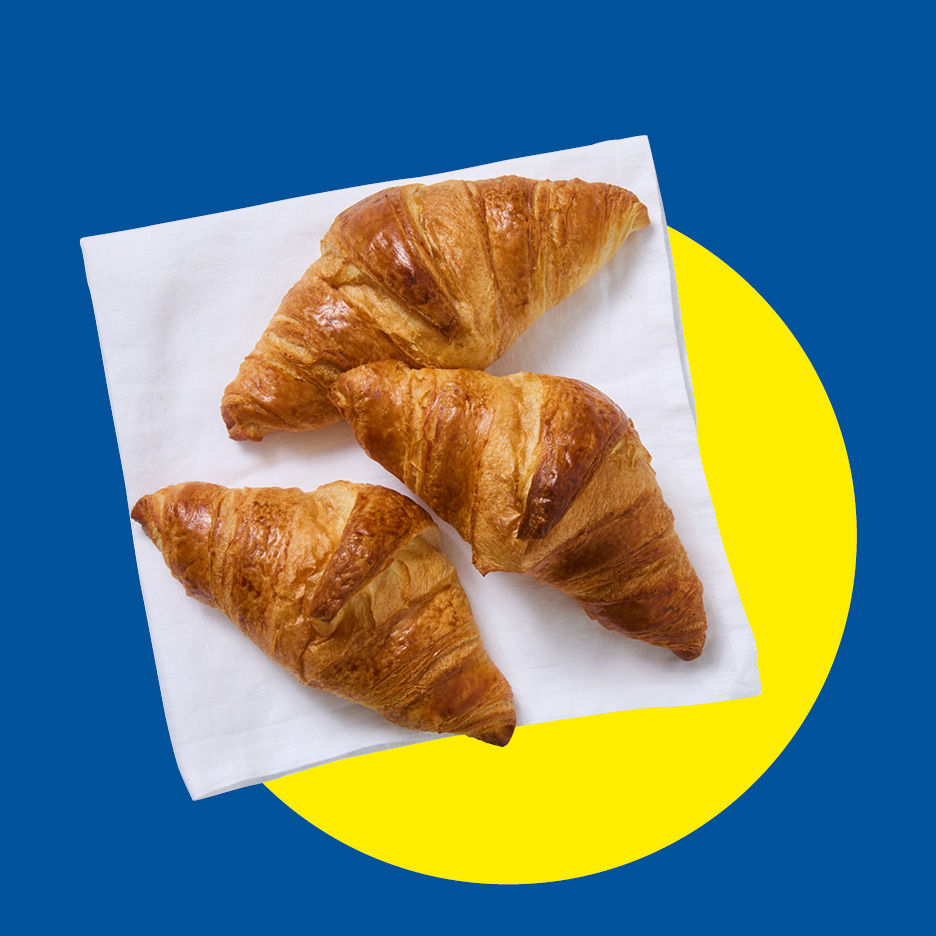 Tre croissant dorati su un tovagliolo bianco, su sfondo blu e giallo.
