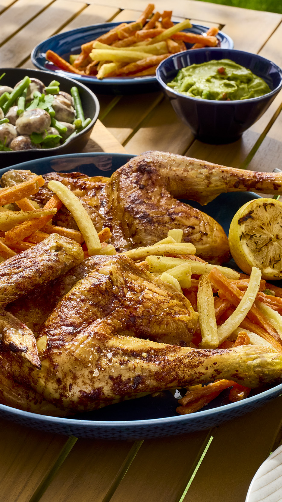 Pollo arrosto con patatine fritte, fagiolini e funghi, e guacamole su un tavolo di legno.