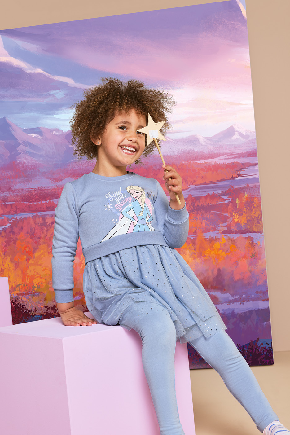 Bambina sorridente con vestito azzurro a tema principessa e bacchetta magica.