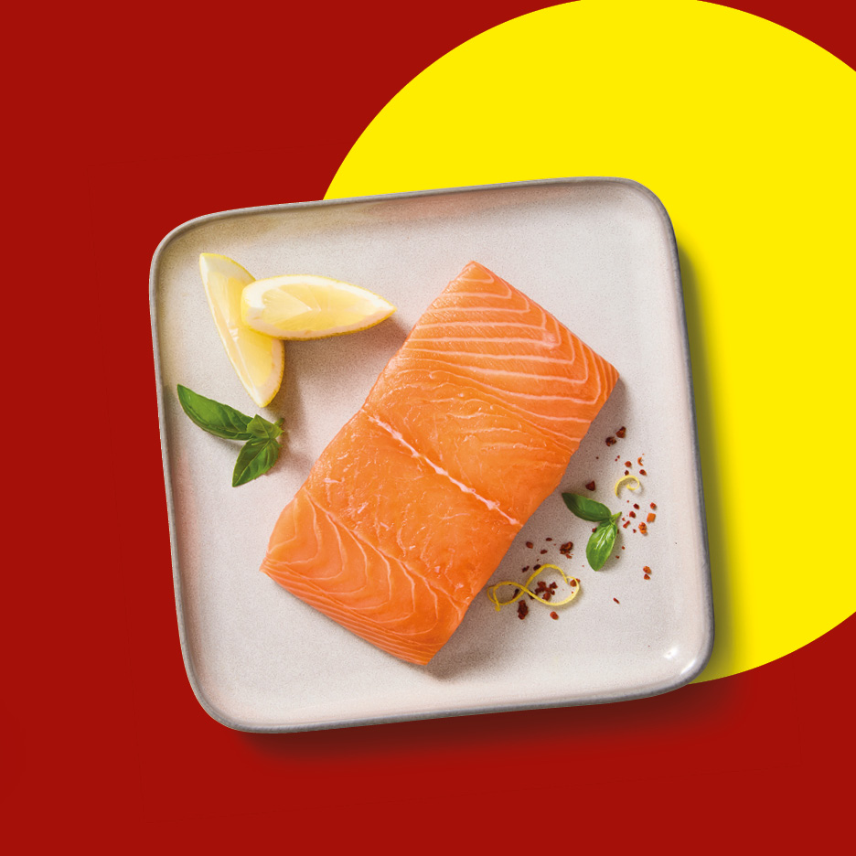 Filetto di salmone fresco servito su un piatto con spicchi di limone, foglie di basilico e spezie.