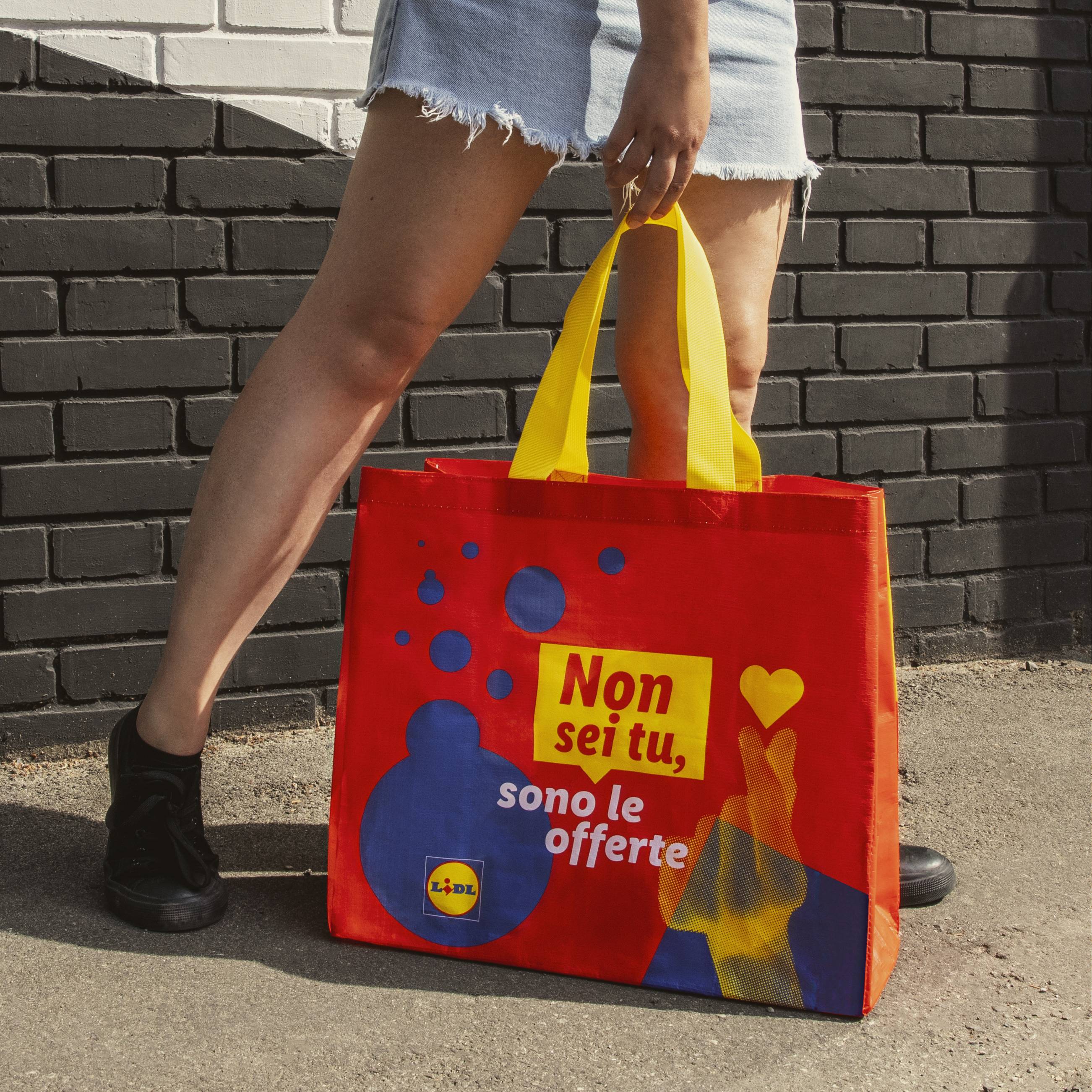 Una donna con una borsa della spesa Lidl di colore rosso e giallo.